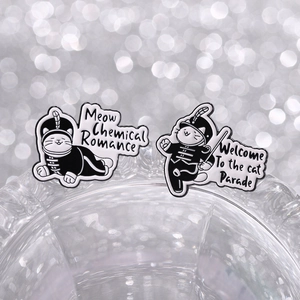 Detail showing two cat enamel pins in marching band uniforms with glittery background
