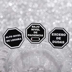 Three black octagonal charms with Spanish text on glass against a bokeh silver background