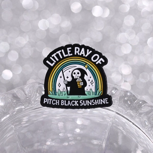 Détail macro du pin's faucheuse avec le texte Little Ray of Pitch Black Sunshine