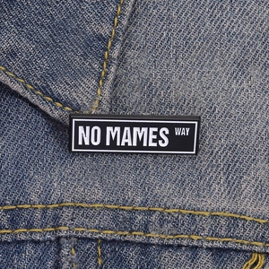 Creative black enamel pin with NO MAMES WAY slogan on a blue denim jacket