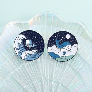 Macro shot of blue enamel whale pins with moonlit waves and starry sky details
