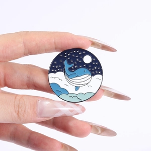 Handheld round enamel pin featuring a blue whale jumping over clouds and moonlight scenery