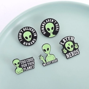 Detail of five funny green alien enamel pins with creative slogans on a ceramic tray