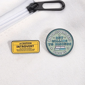 Detail of enamel lapel pins with Introvert and Book Lover quotes on white canvas background
