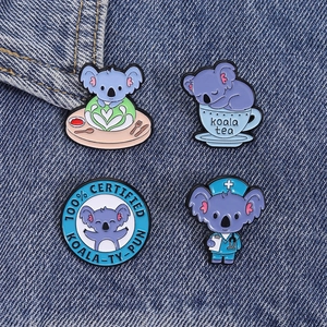 Close-up of four cute koala enamel pins on denim, featuring medical and tea designs