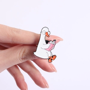 Detailed view of an enamel goose brooch with glasses and pink book held by fingers