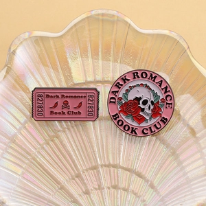 Detailed close-up of pink Dark Romance Book Club enamel pins with skull and rose motifs