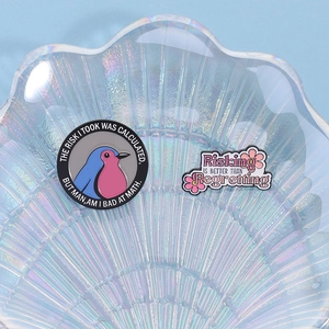 Detail view of colorful enamel pins with bird and flower slogans on a shell tray