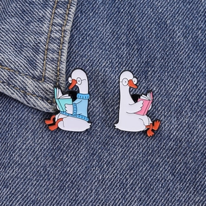Cute enamel goose reading badges with glasses on blue denim fabric background