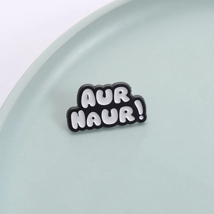 Minimalist enamel brooch with black and white AUR NAUR lettering on green ceramic plate