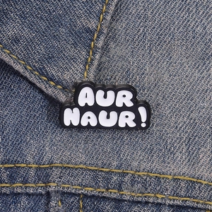 Creative AUR NAUR slang enamel pin in black and white on blue denim jacket