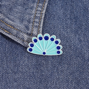 Detail of peacock feather enamel pin with blue gradient on a dark denim jacket texture