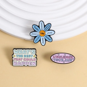Détail de pin's en émail aux motifs floraux et citations inspirantes en tons pastels