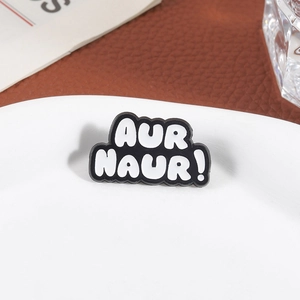 Creative black and white AUR NAUR enamel pin badge accessory on a white plate