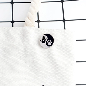 Round enamel yin yang pin with paw and hand print on white canvas bag detail