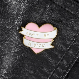 Close-up of pink enamel heart pin with Don't Be A Dick slogan on black leather