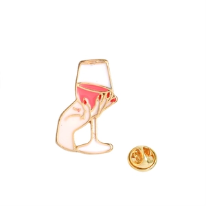 Detailed view of hand holding a pink wine glass enamel pin with a gold butterfly clutch