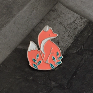 Détail d'une broche en émail renard orange avec motifs de feuilles sur fond de pierre