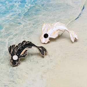 Detail of yin-yang koi enamel pins set on a decorative beach background water ripple