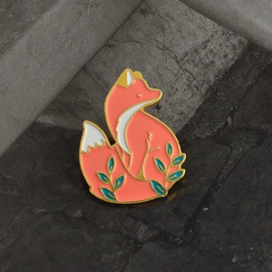Vue macro d'une broche renard en émail avec finition corail et détails de feuilles dorées