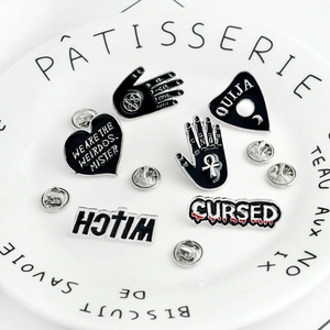 Gothic Ouija hand and witch heart enamel pins set on a white decorative dish