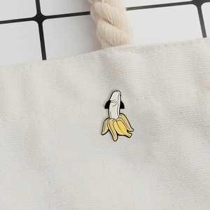 Detailed close-up of a funny banana enamel pin attached to a white canvas bag