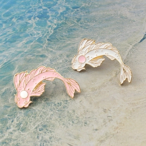Pink and white koi fish enamel pins with gold trim on a blue water-themed background