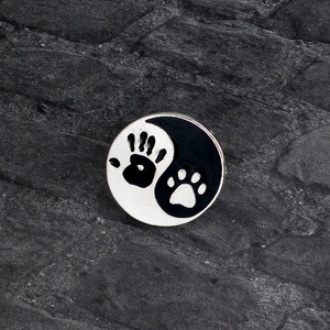 Yin Yang paw and hand print enamel brooch made of metal alloy on a dark rock background
