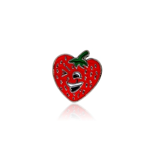 Dettaglio di una spilla in smalto a forma di fragola con viso ammiccante e foglie verdi