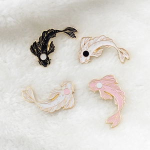 Macro view of koi fish enamel pins in black, white, and pink on soft plush background