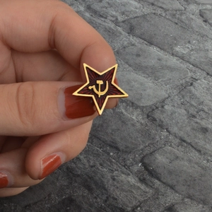 Communist red star badge with golden hammer and sickle symbol held in hand on stone back