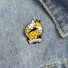 Detail of yellow enamel fox brooch with MISCHIEF flag text on denim fabric background