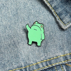 Close-up of a green frog enamel pin attached to a blue denim jacket as a fashion accessory