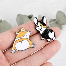 Close-up of two enamel corgi dog pins with glossy metal finish on a hand