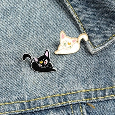 Detailed view of Luna and Artemis cat enamel pins on blue denim fabric background