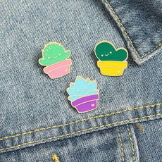 Detailed view of three cartoon succulent enamel pins on a blue denim jacket pocket