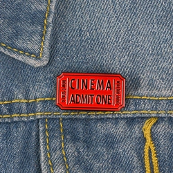 Épingle émaillée en forme de ticket de cinéma rouge sur une veste en jean bleue