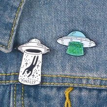 Detailed view of UFO enamel pins with FINALLY text and glitter cool design on denim fabric