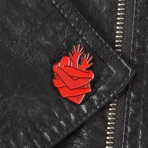 Macro shot of a red heart-shaped hands hugging enamel pin on a black leather jacket lapel