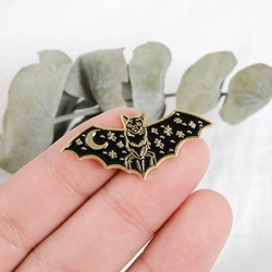 Détail d'une main tenant une broche chauve-souris en émail noir avec lune dorée