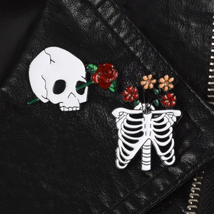 Gothic skull with red rose and rib cage enamel pins on a black leather jacket detail