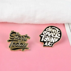 Détail des badges émaillés Start Today et Don't Over Think It sur un fond rose moderne