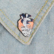 Detailed view of creative anatomical heart enamel pin on light blue denim jacket fabric