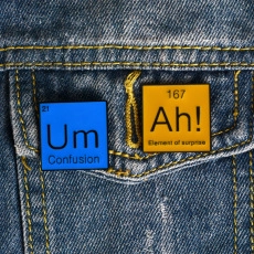 Detail of square enamel pins with chemical elements Um and Ah on denim jacket pocket