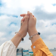 Photo lifestyle en plein air montrant deux mains avec bracelets de perles sur fond de ciel