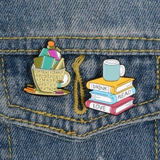 Close-up of enamel book and coffee cup brooches pinned on a blue denim jacket pocket