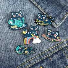 Detail of five space cat enamel pins featuring planets and rainbow on denim fabric