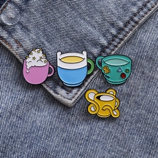 Detail of four cartoon enamel pins featuring Adventure Time character cups on denim fabric