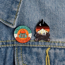 Macro view of outdoor enamel pins set featuring campfire and mountains on denim jacket