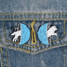 Detail of creative blue and white enamel pins showing an animal jumping through portals